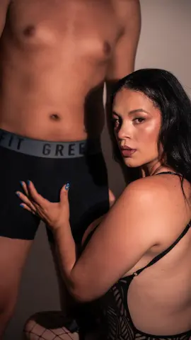 Young woman in black lace lingerie posing intimately with a shirtless man in a moody studio setting.