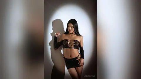 Glamorous woman in a black lace cutout crop top and mini skirt posing under dramatic studio spotlighting.