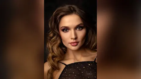 Glamorous woman with wavy brunette hair and smoky eye makeup wearing a black sequined evening top.
