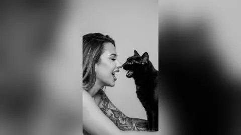 AvaBronX — AvaBronX smiles while looking at a black cat in this black and white portrait.