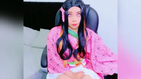 HimeJess wears a pink patterned kimono and has long black hair with orange highlights while sitting in a black chair.