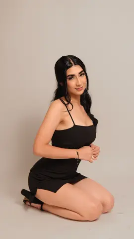 Young woman in a black mini dress posing elegantly against a neutral studio background.