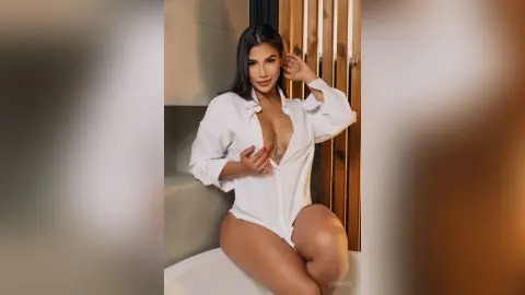 Beautiful woman in an oversized white button-down shirt posing in a modern bathroom setting.