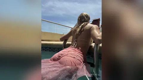 MielVerane shows her wet, blonde hair and bare back while sitting on a pool ladder in a pink lace bikini or cover-up.