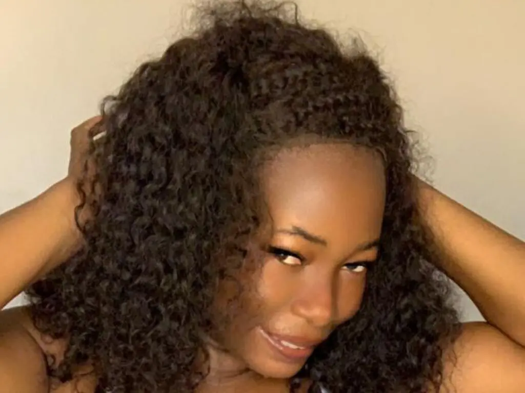Beautiful woman with voluminous curly dark hair smiling in a soft, natural indoor setting.