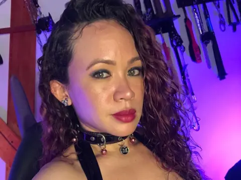 Woman with curly hair wearing a black choker and dark makeup in a moody purple lit room.