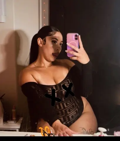 Woman in a black patterned bodysuit taking a mirror selfie in a dimly lit room.