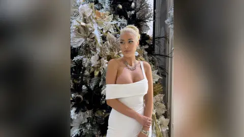 Elegant woman in a white cocktail dress posing by a glamorous silver and gold floral arrangement.