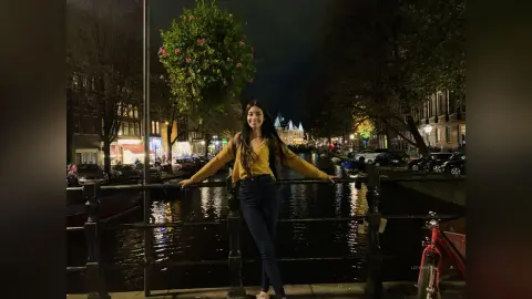LucyMartin stands by a canal at night wearing a yellow long-sleeved top and dark blue jeans.