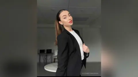 Elegant woman in a black blazer and white top posing confidently in a modern minimalist room.