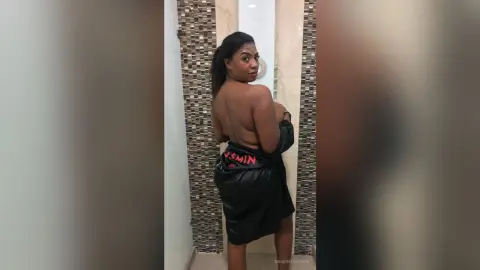 NahomyBrown poses with her back turned, wearing a black satin robe that slips down to show her bare back and shoulders.