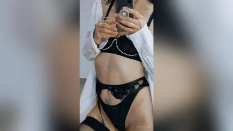 Woman in black lace lingerie and white robe taking a mirror selfie in a bright room.