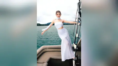 Elegant woman in a white summer maxi dress posing on a boat against a scenic ocean backdrop.