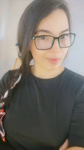 Smiling young woman with glasses wearing a black t-shirt in a bright indoor setting.