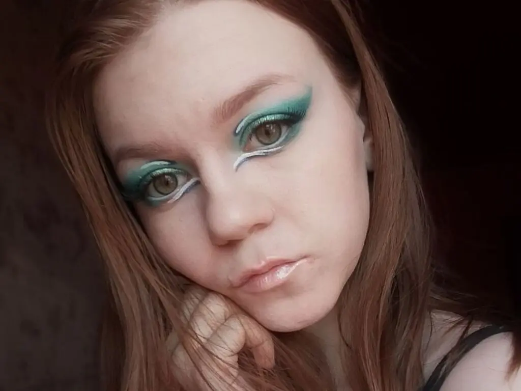 Close-up portrait of a woman with dramatic teal winged eyeliner and fair skin in soft natural lighting.