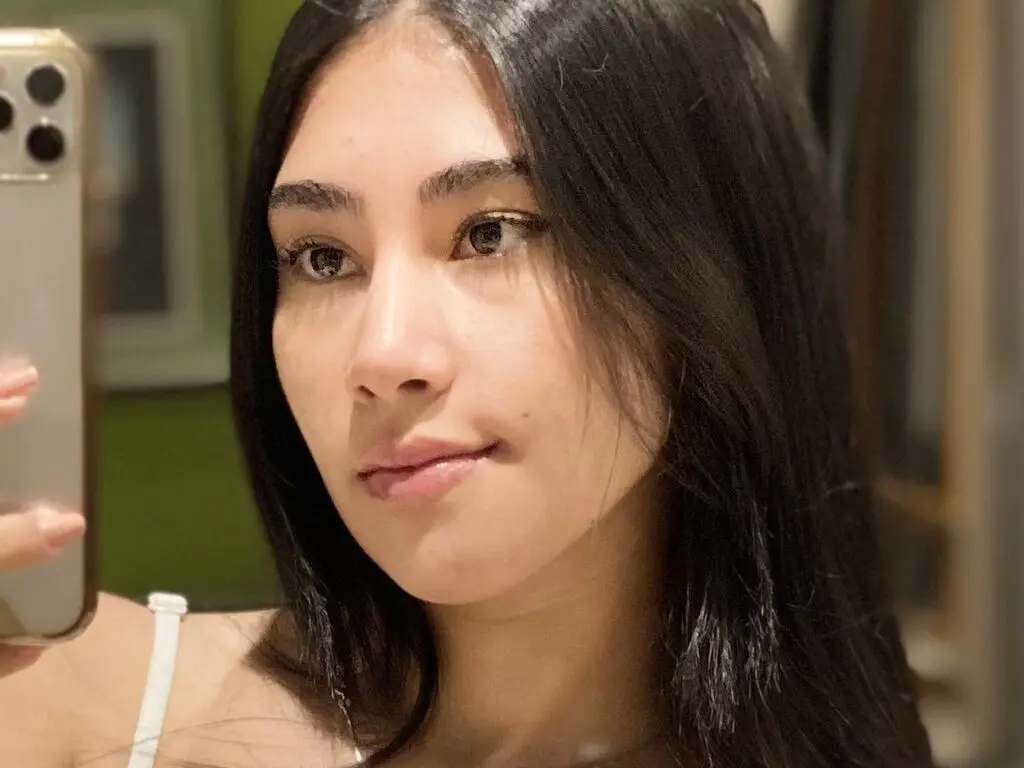 Young woman with long dark hair taking a close-up selfie in a warm indoor setting.
