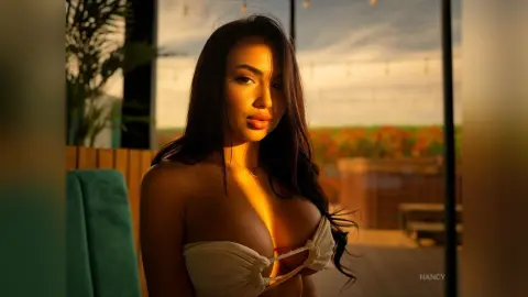 Beautiful woman in a white strapless top posing in warm sunset lighting at an outdoor rooftop lounge.