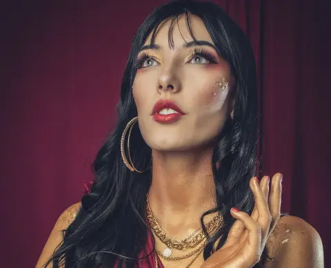 Glamorous woman with dark hair and gold makeup posing against a deep red backdrop in a moody, elegant style.
