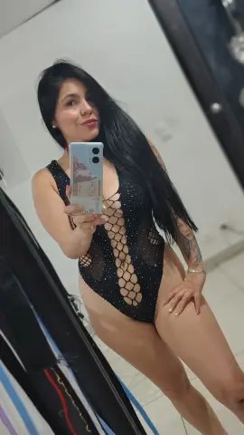 Woman in a black sparkly cutout bodysuit taking a confident mirror selfie in a modern room.