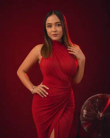Elegant woman in a red evening gown posing against a dark red background for a sophisticated portrait.