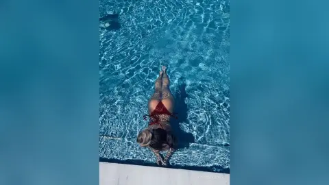 KendallMinx lies on her stomach in a clear blue swimming pool wearing a tiny red bikini.
