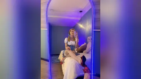 Young woman in a white puff-sleeve blouse taking a mirror selfie in a moody, blue-lit bedroom.