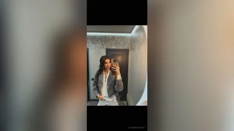 CatherineThomase — CatherineThomase takes a mirror selfie wearing a grey jacket over a white top and white pants.
