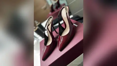 Elegant burgundy patent leather high heel pumps with crystal embellished straps on a luxury display stand.