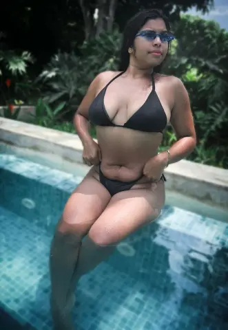 Young woman in a black bikini relaxing in a tropical swimming pool on a sunny summer day.