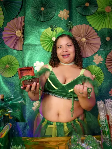 Smiling woman in a green leprechaun costume holding a treasure box at a festive St. Patrick's Day party.