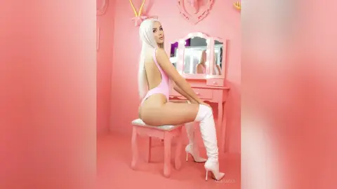 Blonde woman in a pink bodysuit and white thigh-high boots sitting in a dreamy pink aesthetic room.