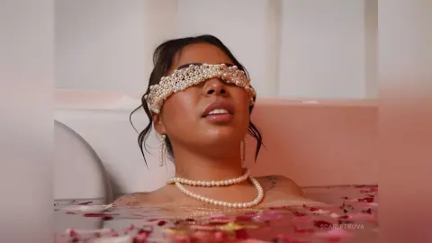 Serene woman with pearl headband and necklace relaxing in a rose petal bath for a dreamy aesthetic mood.