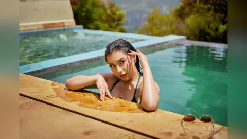 Young woman in a dark bikini relaxing by a luxury infinity pool overlooking a scenic mountain landscape.