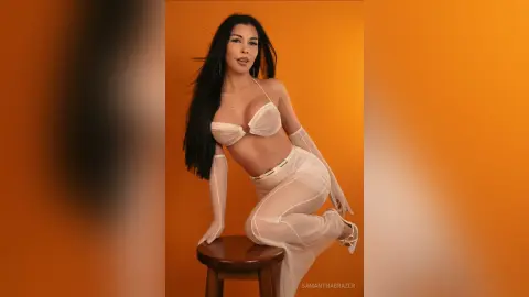Glamorous woman in a white bikini and sheer gloves posing against a vibrant orange background.