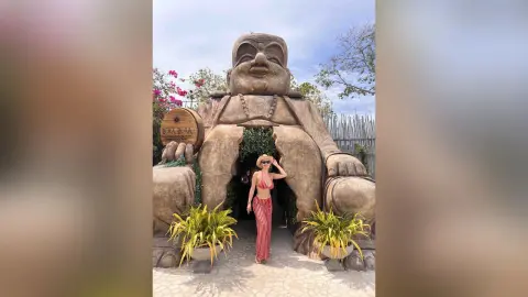 Woman in a red bikini and striped pants posing in front of a giant Buddha statue at Bora Bora Beach Club.