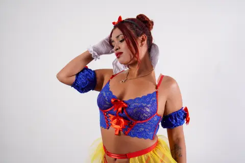 Woman in blue lace Snow White cosplay outfit with red bow and yellow skirt posing against a white background.
