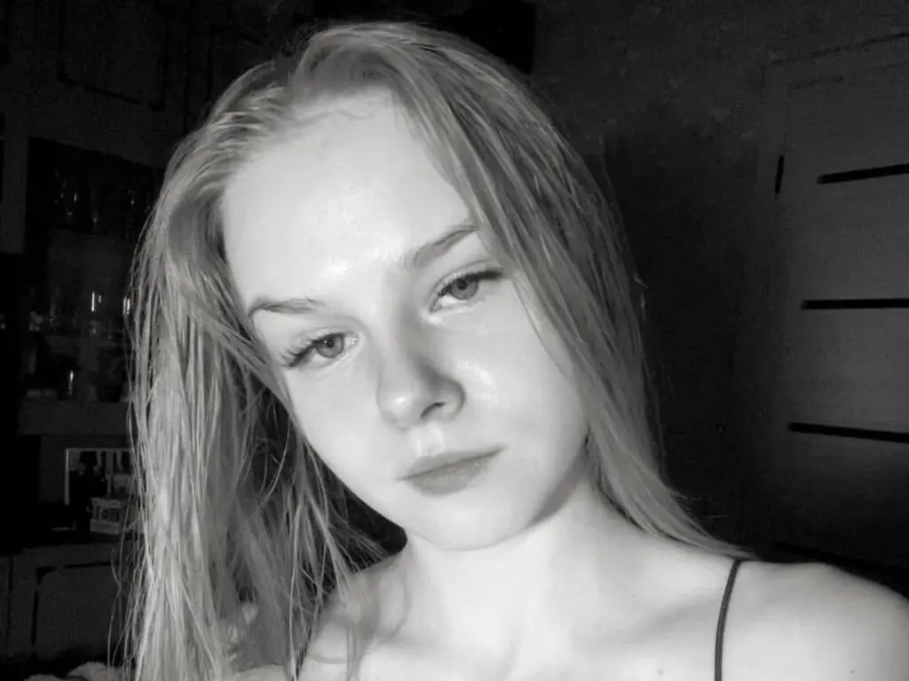 Close-up portrait of a young woman with long blonde hair in a moody black and white indoor setting.