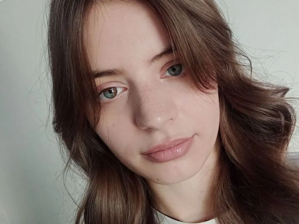 Close-up portrait of a young woman with long brown hair and green eyes looking calmly at the camera.