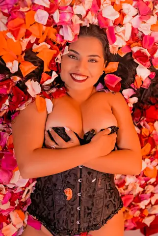 Smiling woman in black lace lingerie lying amidst a romantic bed of red and orange rose petals.