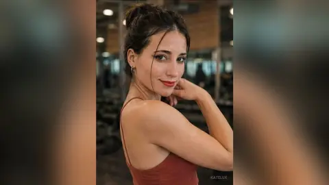 Smiling young woman in a red tank top posing in a modern gym setting with a confident mood.