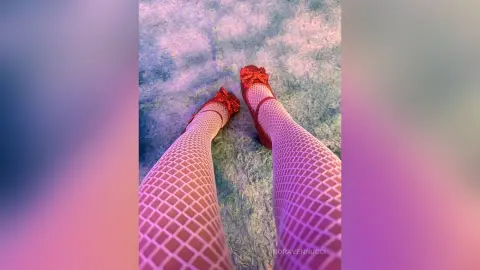 Close-up of legs in white fishnet tights and red glitter heels resting on a soft blue textured rug.