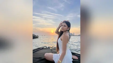 Young woman in a white sundress enjoying a peaceful sunset on a boat at sea.