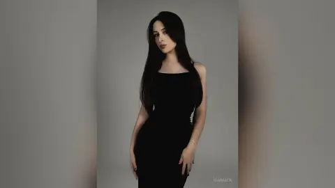 Elegant woman in a sleek black cocktail dress posing against a minimalist grey studio background.