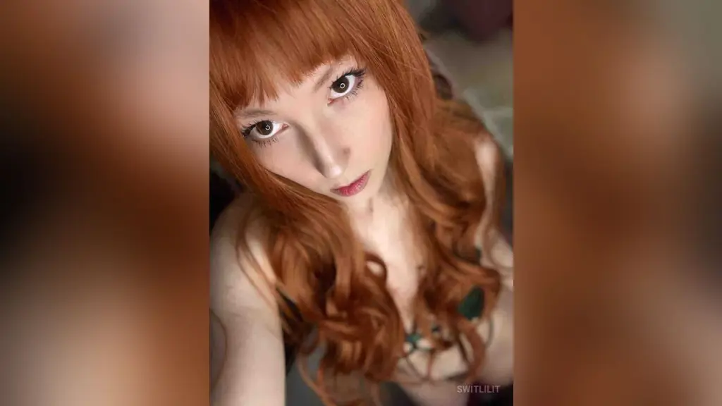 SwitLilit — Redheaded woman with long wavy hair posing in a dark green lace outfit for a moody portrait.
