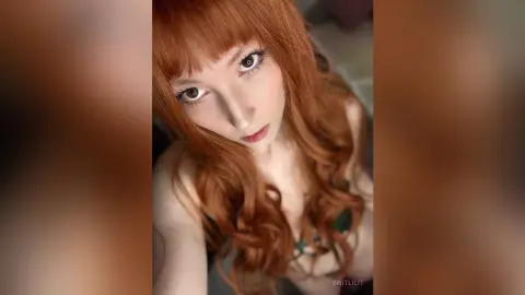 Redheaded woman with long wavy hair posing in a dark green lace outfit for a moody portrait.