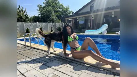 Woman in a green bikini relaxing by a sunny outdoor swimming pool with a large dog.