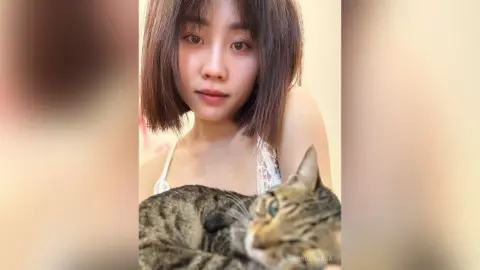 Young woman in a white lace top cuddling a tabby cat in a cozy indoor setting.