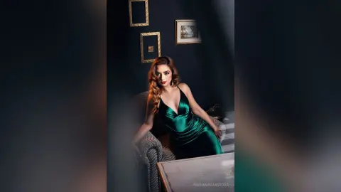Elegant woman in a glamorous emerald green satin gown sitting in a moody, dark-toned luxury interior.