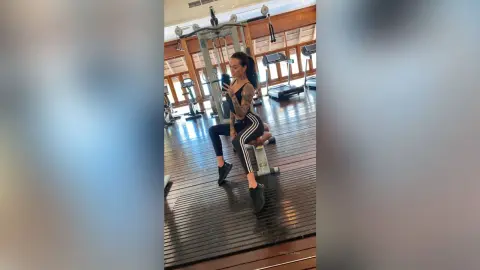 Tattooed woman in black gym wear taking a selfie in a modern home fitness studio.
