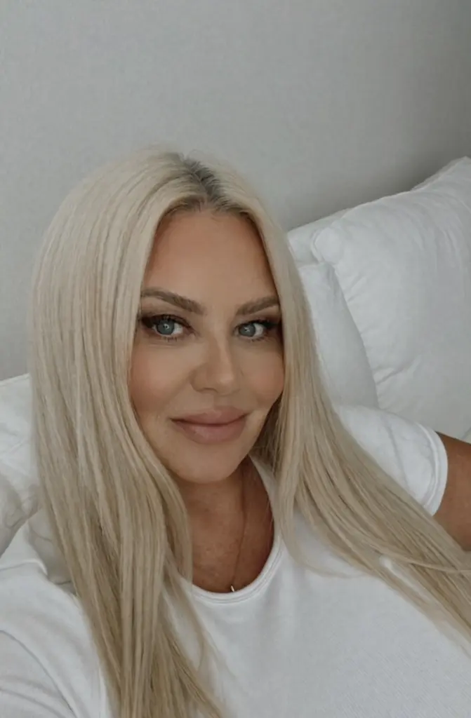 MollySwedeXO is a blonde woman wearing a white blondie t-shirt and grey leggings, holding a glass of champagne in a kitchen.